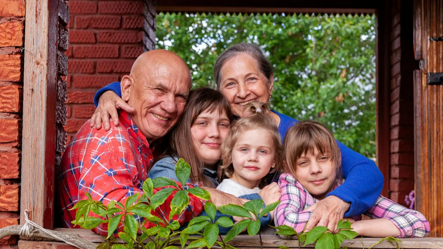 Grandparents, their daughter and grandchildren smiling together at an open window