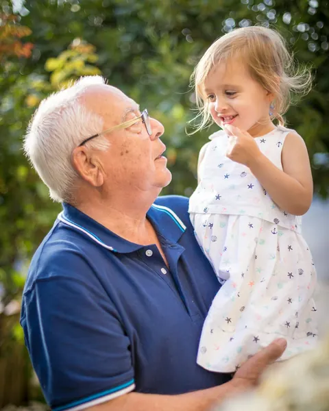 A grandfather holding his young granddaughter in a garden